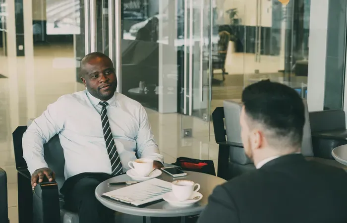 Two professionals discuss documents over coffee in a modern lounge, tablets and notes during an informal meeting
